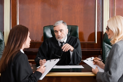 senior-judge-holding-eyeglasses-near-attorney